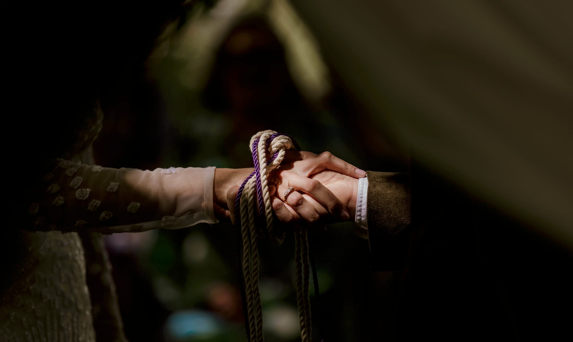 Handfasting cords bound around a couple's joined hands during a Cornwall wedding ceremony