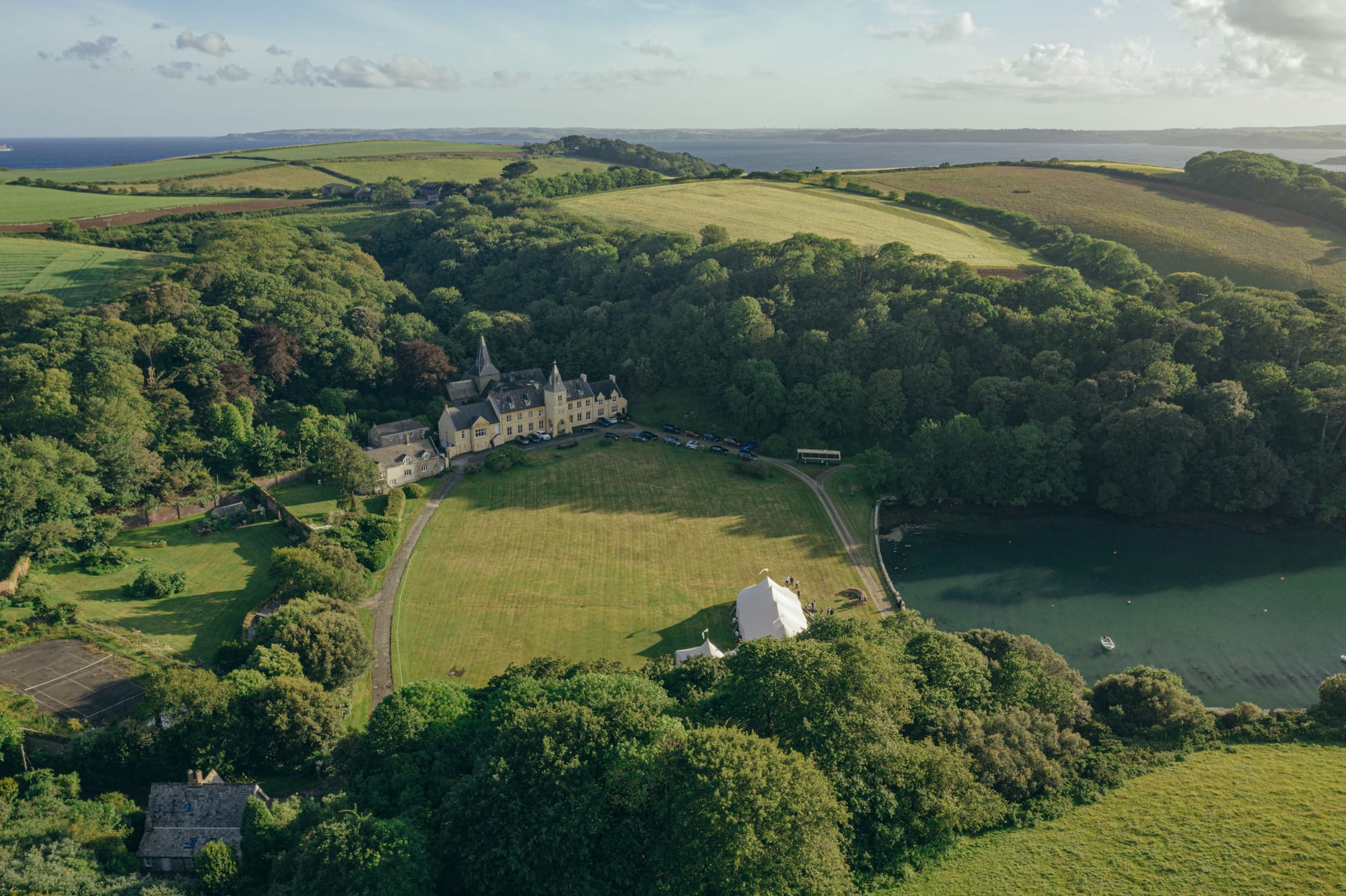 The whole stage from above — house, marquee, creek, the sea beyond.